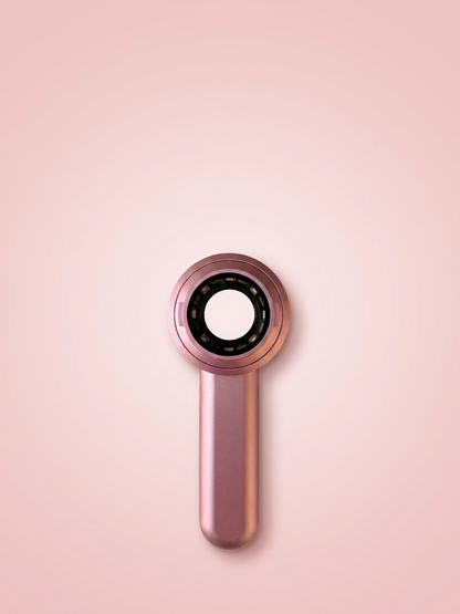 A handheld SkinLens Pink Dermatoscope with a metallic pink finish, featuring a circular head with a black inner ring and a central white opening, set against a solid light pink background.
